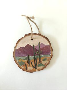 a wooden ornament hanging on a string with mountains in the background and cactus trees