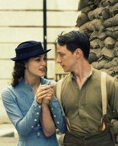 a man and woman standing next to each other in front of a wall with bags on it