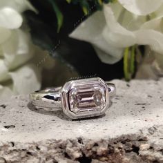 an emerald cut diamond ring sitting on top of a rock