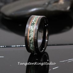 a wedding band with green moss inlays is shown on top of a black surface