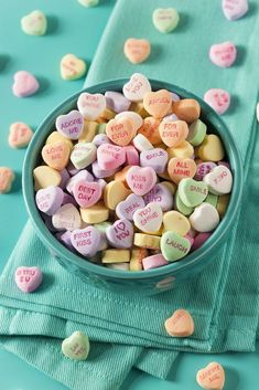 a bowl filled with conversation hearts on top of a blue cloth next to green napkins