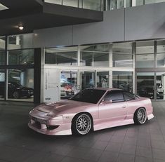 a pink sports car parked in front of a building with glass doors and large windows