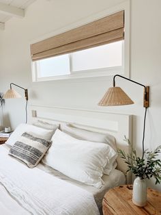 a bed with white linens and pillows in a small room next to a window