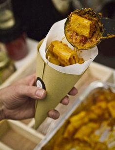 a person holding an ice cream cone filled with food next to a tray of other foods