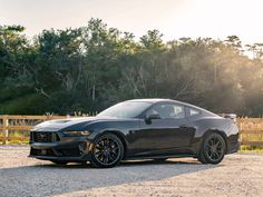 a black sports car is parked in front of a wooden fence and grassy area with trees