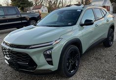 the front end of a light green suv parked in gravel with other cars behind it