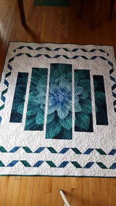 a quilted table runner with blue and green flowers on the top, sitting on a wooden floor