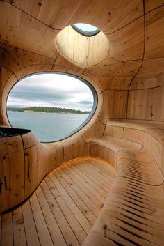 the inside of a wooden boat looking out at water and land through a round window