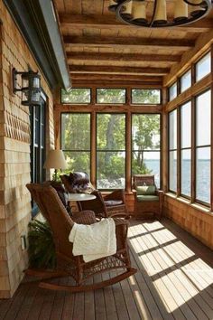 a porch with rocking chairs and windows overlooking the water is shown in this photo from inside