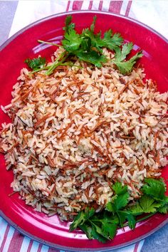 a red plate topped with rice and cilantro on top of a striped table cloth