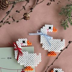 two cross stitch sheep ornament hanging on a tree branch with pine cones in the background