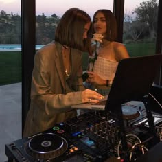 two women standing next to each other in front of a dj's equipment