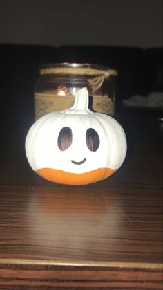 a pumpkin with a face painted on it sitting on a table next to a jar