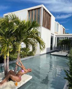 a woman laying on the edge of a swimming pool next to a palm tree in front of a house