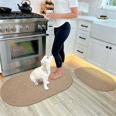 a woman standing in front of an oven with a white dog on the floor next to it