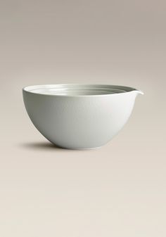 a white bowl sitting on top of a table next to a gray wall and floor