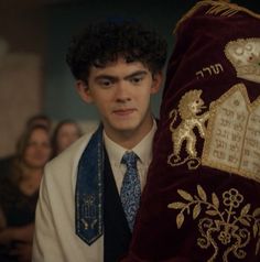 a young man in a white shirt and blue tie holding up a red velvet bag