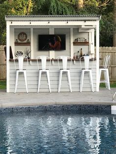 an outdoor bar next to a pool with white chairs and barstools on it