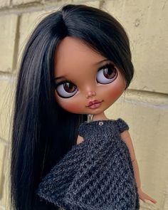 a doll with long black hair wearing a gray dress and holding onto a brick wall