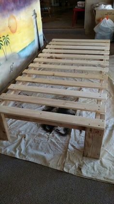 a wooden bed frame sitting on top of a sheet covered floor next to a painting