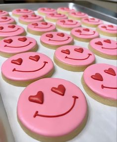 pink decorated cookies with hearts and smiley faces on them are lined up in the middle of a baking sheet