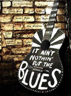 a black and white guitar sitting against a brick wall with writing on it that says, it isn't nothing but the blues