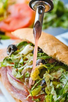 a close up of a sandwich with meat and veggies on it, being held by a faucet