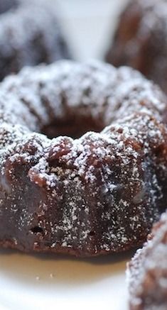 chocolate donuts with powdered sugar on them sitting on a white plate, ready to be eaten