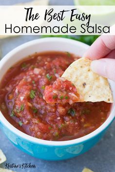 a hand holding a tortilla chip over a bowl of homemade salsa