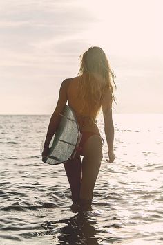 a woman walking into the ocean carrying a surfboard