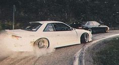 two cars driving down the road with dust coming out of their tires on either side