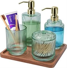 three glass containers with toothbrushes, soap and toothpaste on a wooden tray