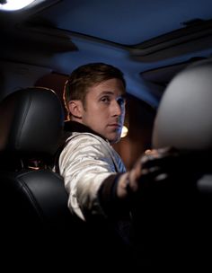 a young man sitting in the driver's seat of a car with his hand on the steering wheel