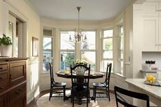 a dinning room table with four chairs in front of two windows and a chandelier hanging from the ceiling