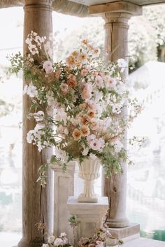 a vase filled with lots of flowers sitting on top of a white table next to columns