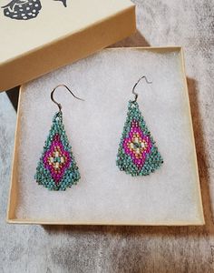 a pair of beaded earrings sitting in a box next to a card board with an ornament on it