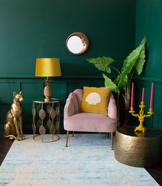 a living room with green walls and gold accents on the rug, pink chair, brass table lamp, and other decorative items