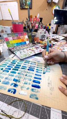 two people are working on an art project with watercolors and pencils in front of them