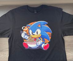 Shirt of your favorite hedgehog enjoying ramen. Shirt is available in black and in sizes small, medium, large and extra large.  Shirt is Gildan brand unisex made out of cotton. Womens Sonic Shirt, Ramen Shirt, Sonic Hedgehog, Gaming Shirt, The Hedgehog, Soft Style, Unisex Shirt, Heat Press, Favorite Things Gift