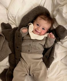 a baby laying on top of a bed wearing a coat