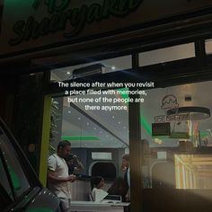 a man standing in front of a store window next to a car and another person sitting at a table