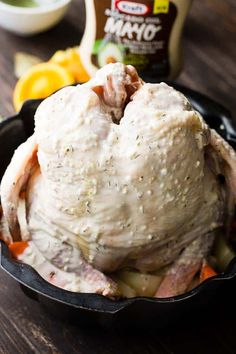 a chicken in a skillet sitting on a table next to oranges and seasoning