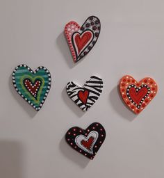 four decorative heart shaped magnets on a white surface, each decorated with different patterns and colors