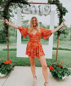 a woman standing in front of a sign with her hands up to the side and smiling