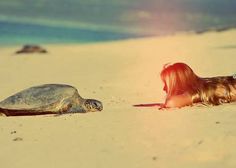 a woman laying on top of a sandy beach next to a turtle