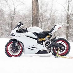 a white motorcycle parked in the snow next to trees