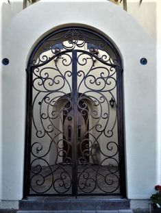 an ornate iron gate is shown in front of a white stucco building with red flowers