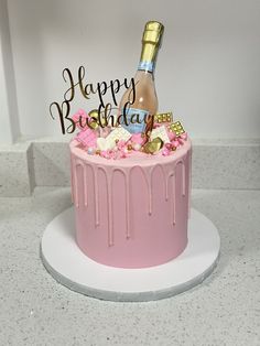 a pink birthday cake with a bottle of champagne and candies on top that says happy birthday