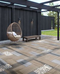 a swing chair and bench on a patio with stone flooring in front of a black building