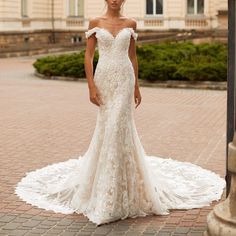 a woman in a white wedding dress standing on a brick walkway with her arms behind her back